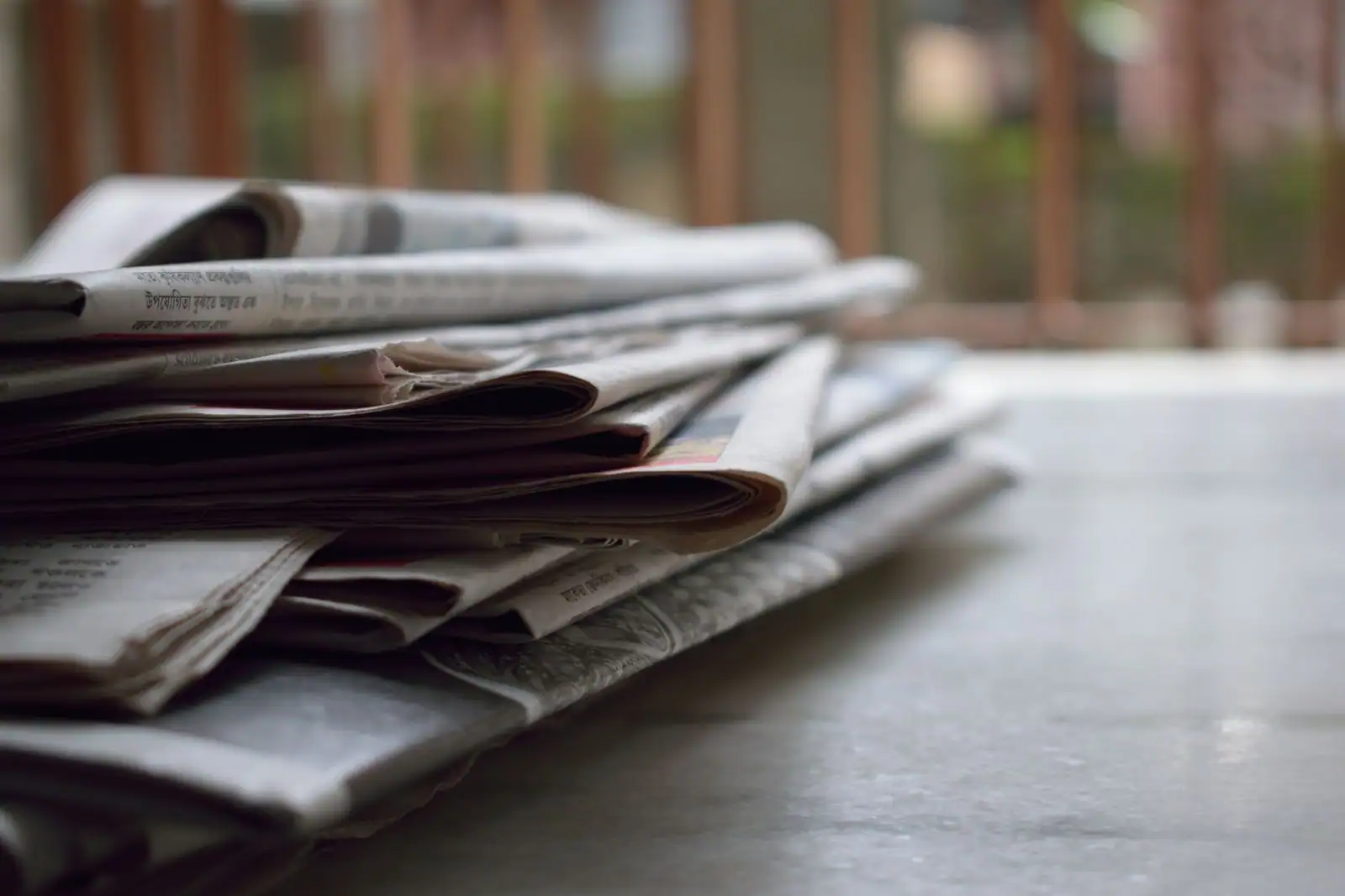 Pile de journaux quotidiens pliés posés sur une surface, devant une fenêtre lumineuse