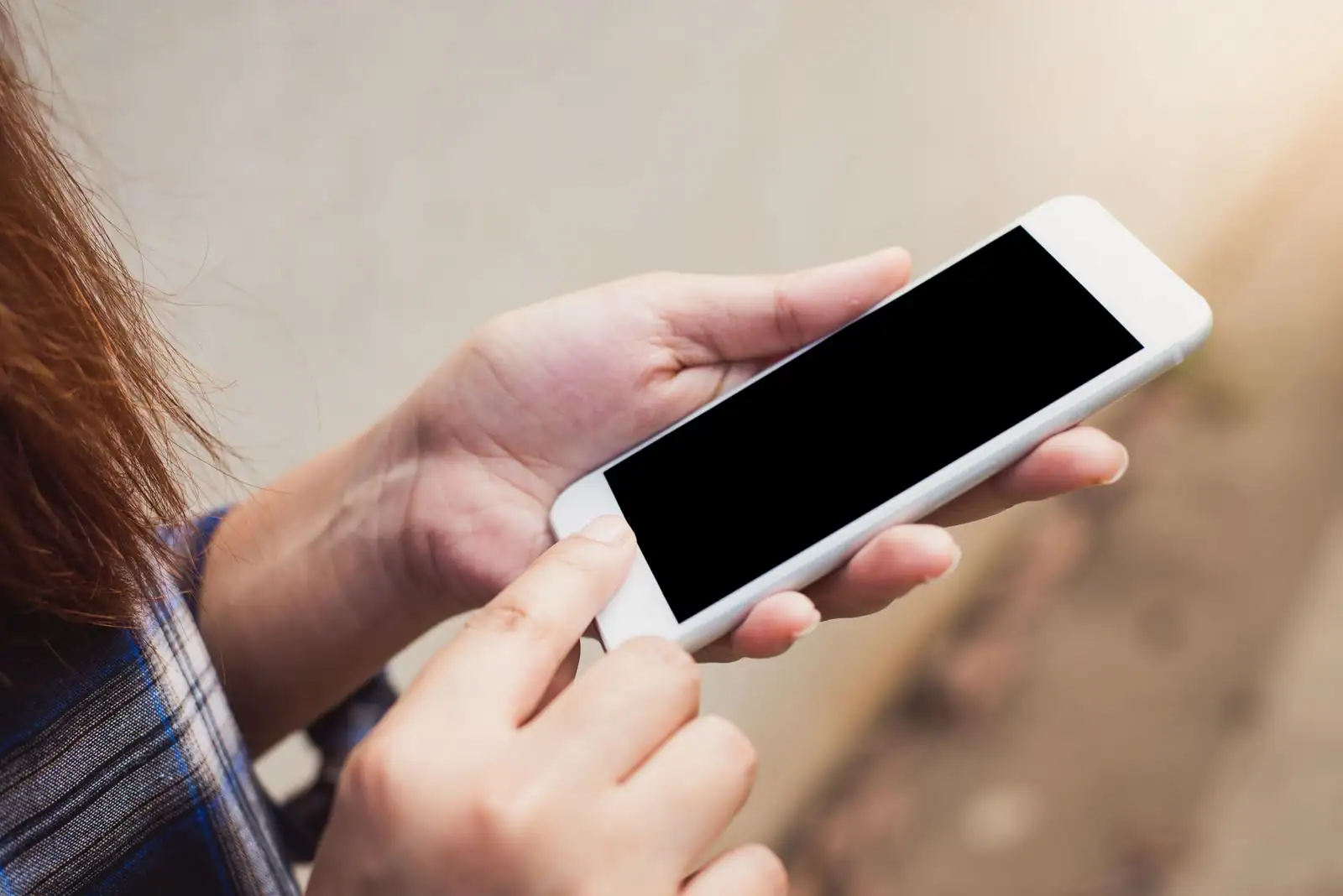 Personne manipulant un smartphone blanc à l'écran vide, tenu à deux mains en extérieur