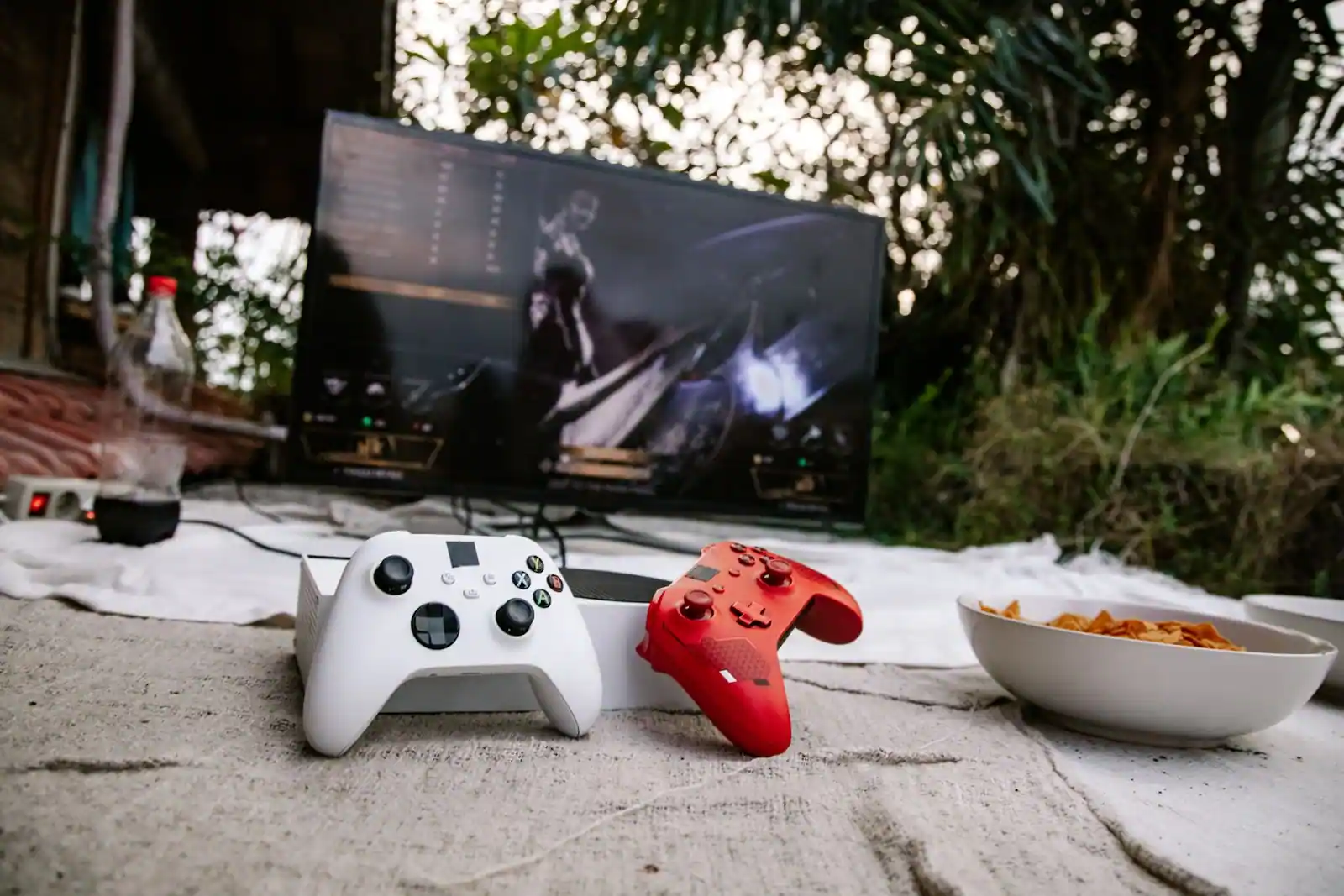 Deux manettes de jeu posées devant un écran de télévision affichant un jeu vidéo, en extérieur
