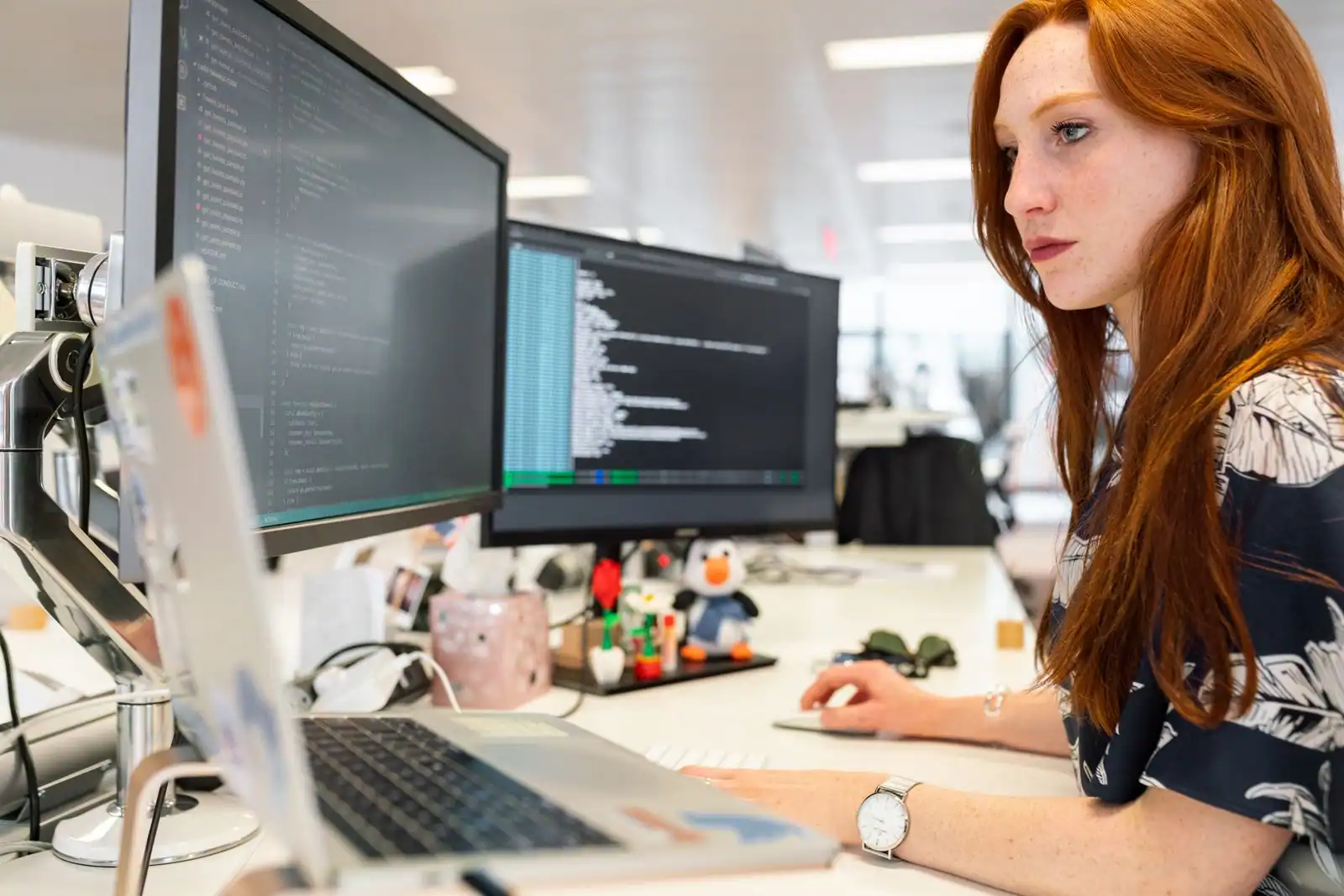 Développeuse web travaillant sur du code affiché sur deux écrans dans un bureau lumineux