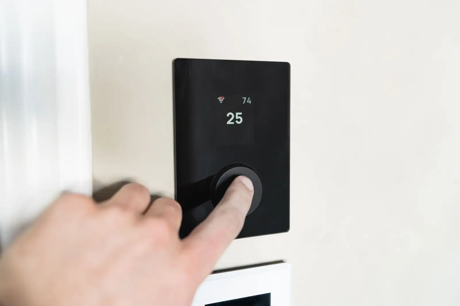 Main réglant un thermostat connecté mural dans un intérieur de maison