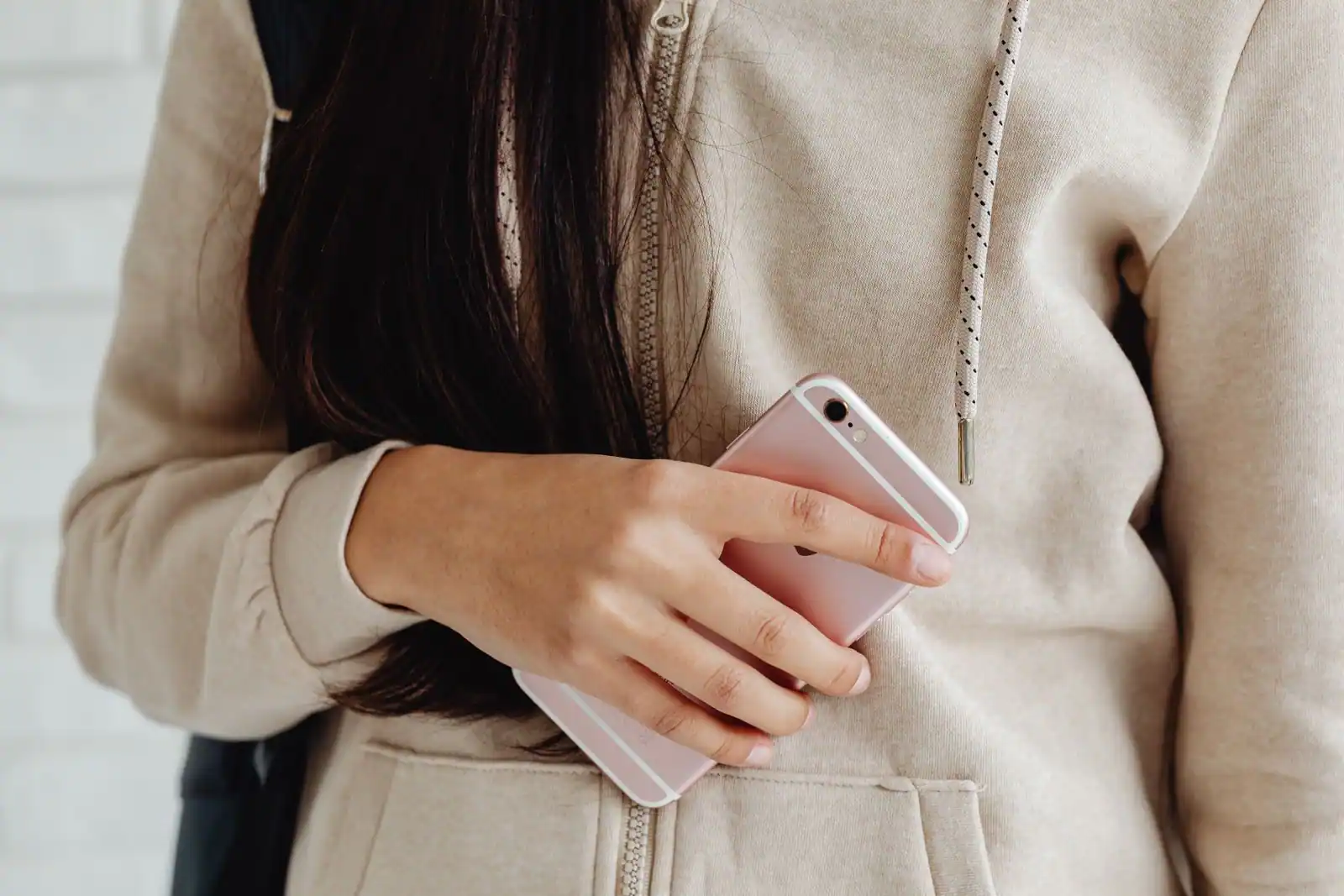 Smartphone rose gold tenu en main et vu de dos, contre un sweat à capuche beige clair.