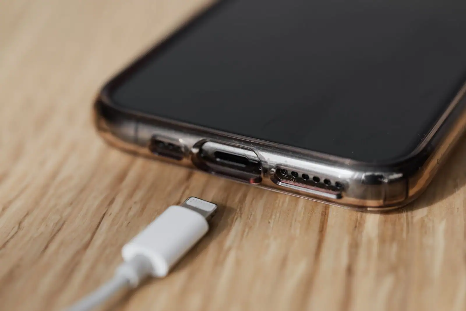 Câble de charge Lightning posé près du port d'un iPhone, sur un bureau en bois clair