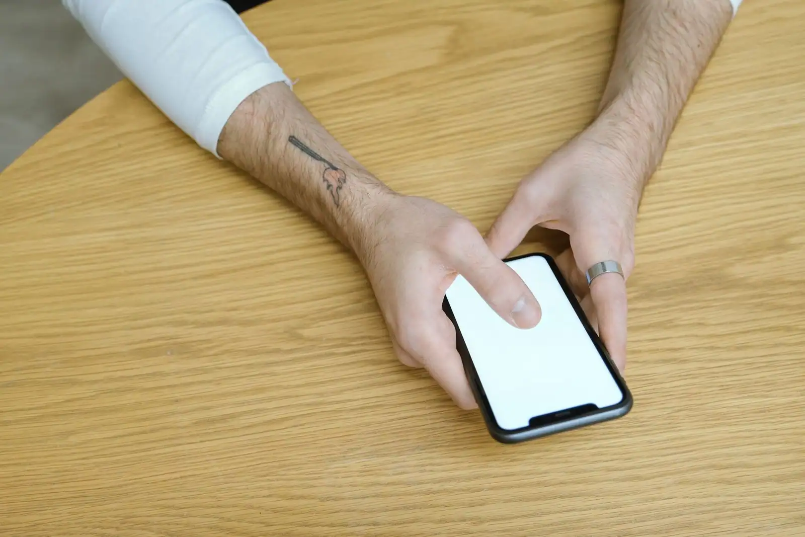 Mains d'une personne manipulant un smartphone à écran blanc, posé sur une table en bois