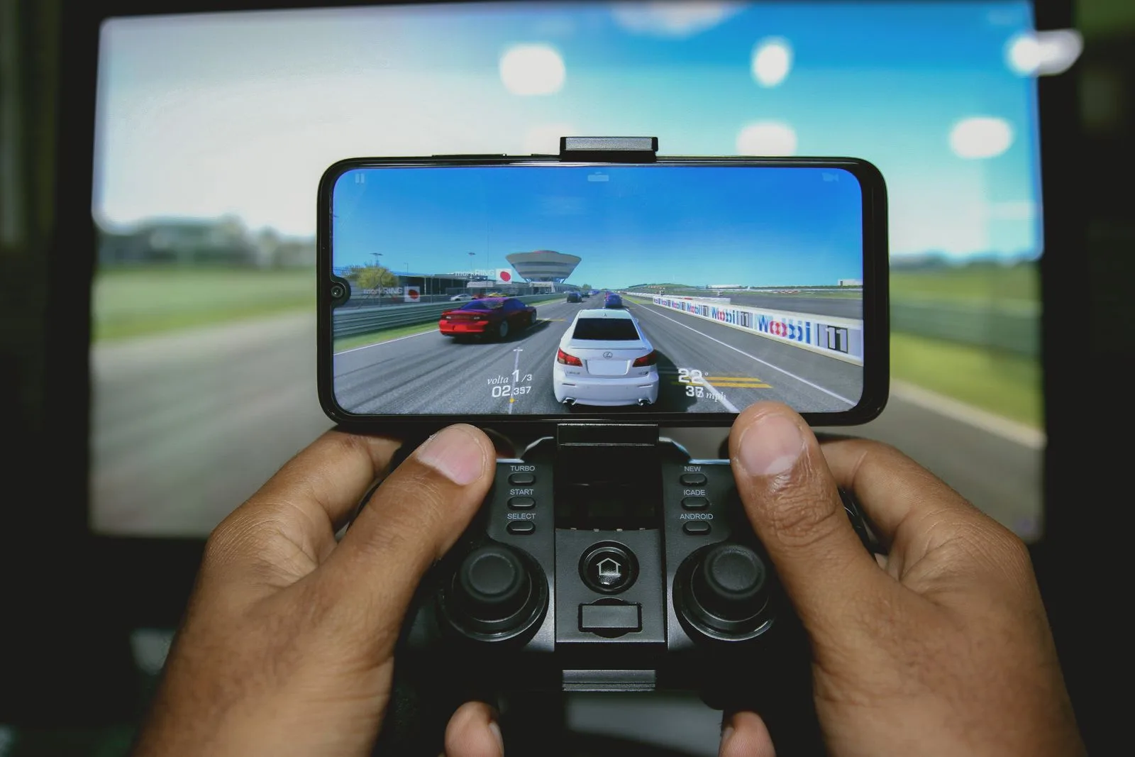 Smartphone fixé sur une manette de jeu, tenu à deux mains, affichant un jeu de course automobile