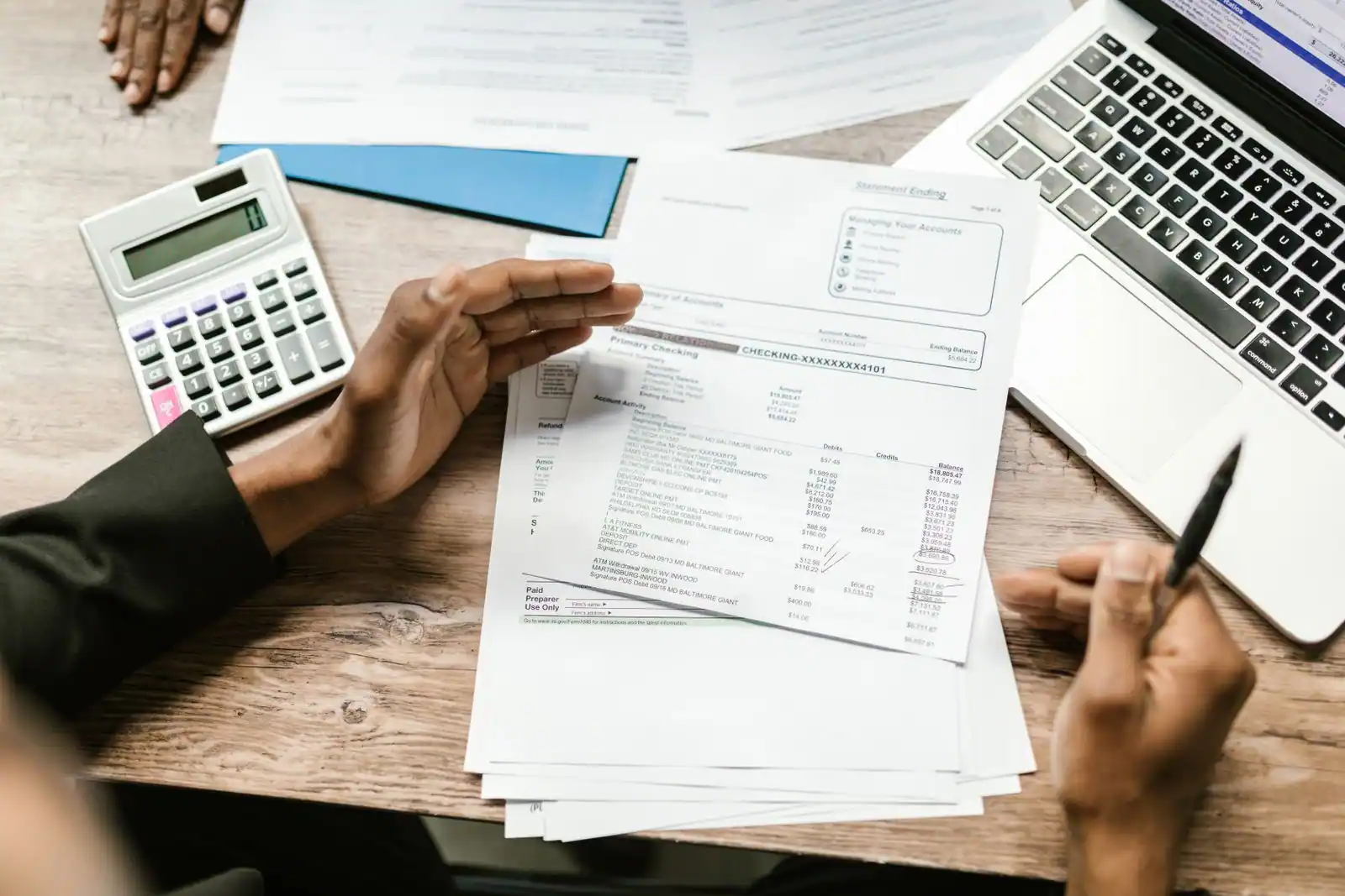 Relevé de compte examiné à la main, avec calculatrice et ordinateur portable sur un bureau