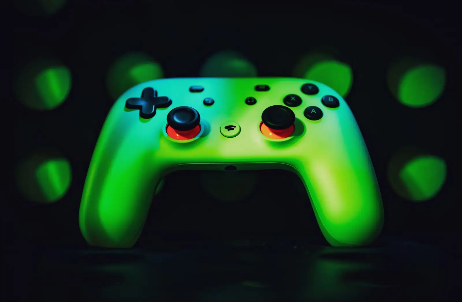Manette de console de jeu posée sur une surface sombre, éclairée par une lumière verte