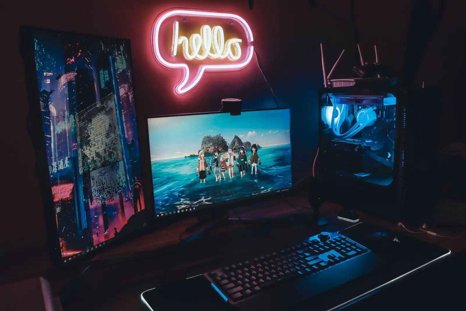 Configuration de jeu sur PC dans une pièce sombre, avec deux écrans allumés dont un affichant un jeu, un clavier et une tour rétroéclairée