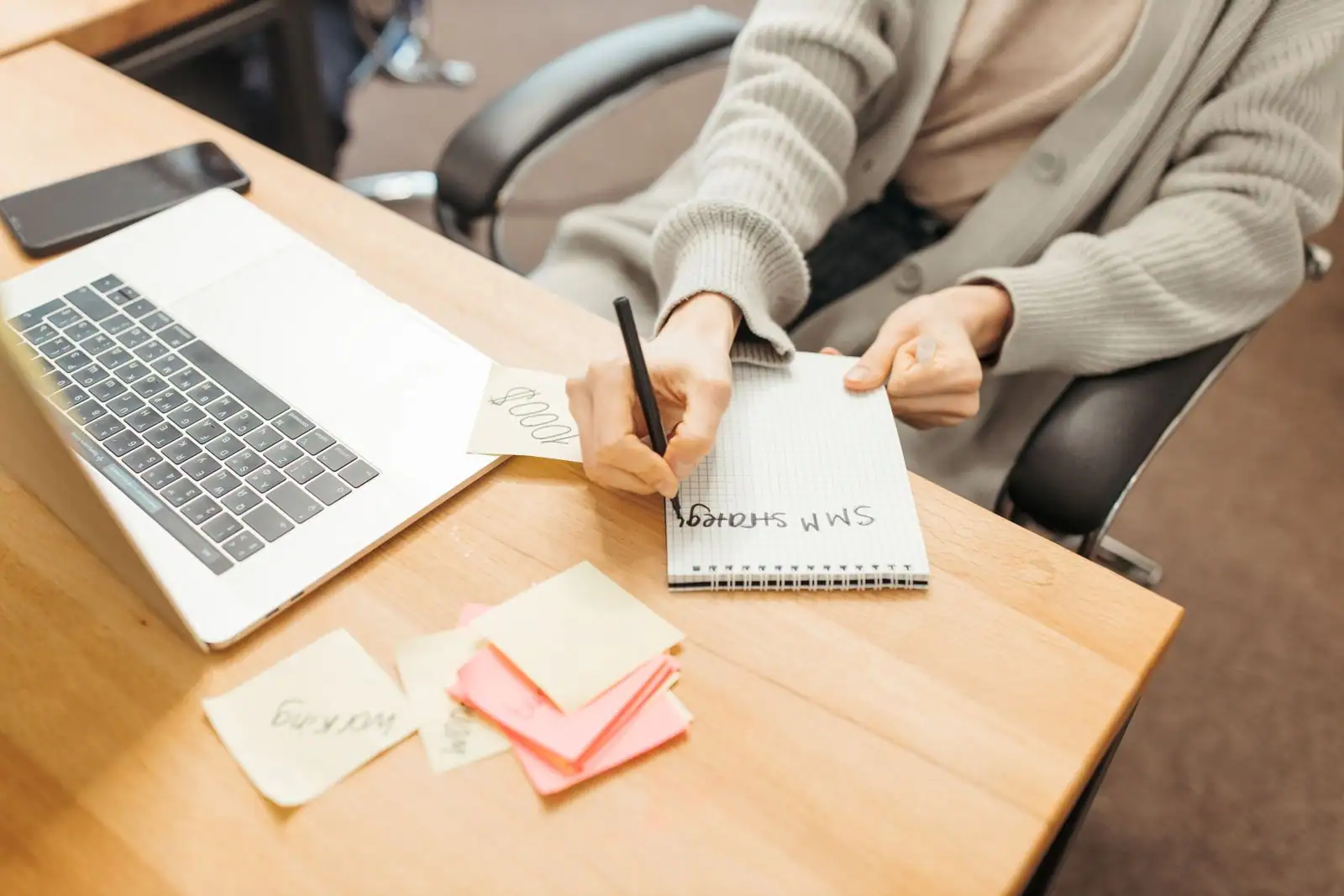 Personne écrivant des notes dans un carnet, à côté d'un ordinateur portable et de pense-bêtes