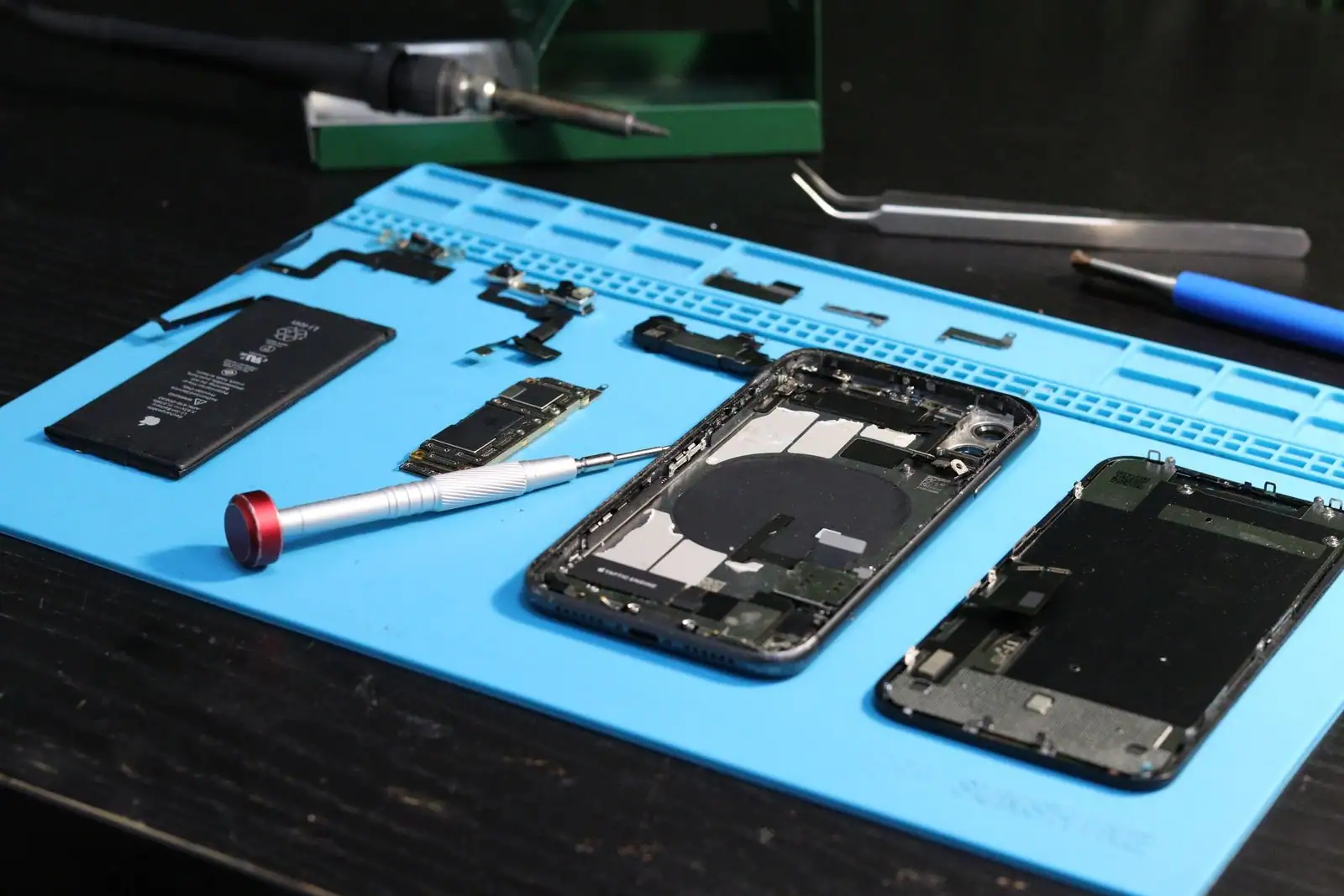 Smartphone démonté avec ses composants et des outils de précision sur un tapis de réparation