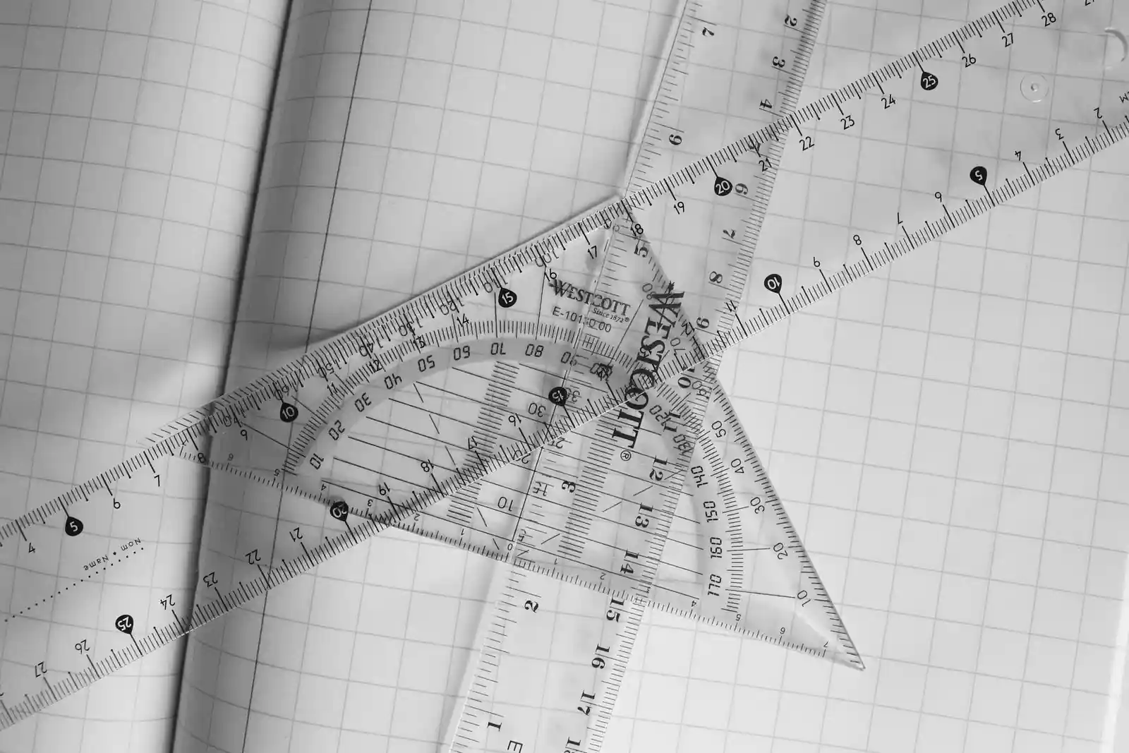 Règles graduées, équerre et rapporteur transparents posés sur une feuille de papier quadrillé