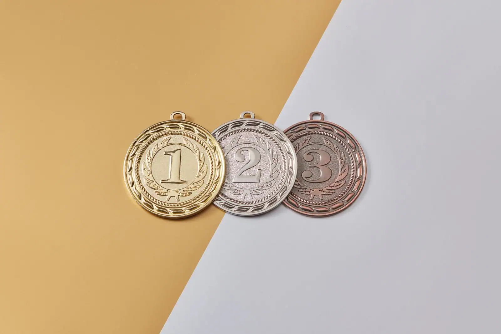 Trois médailles numérotées 1, 2 et 3 — or, argent et bronze — posées sur un fond bicolore jaune et gris.