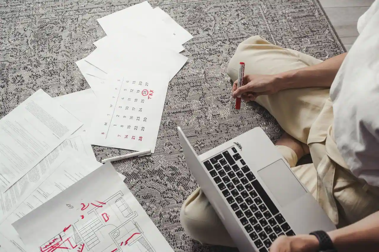 Personne organisant son emploi du temps avec un ordinateur portable, des feuilles de calendrier annotées et des documents