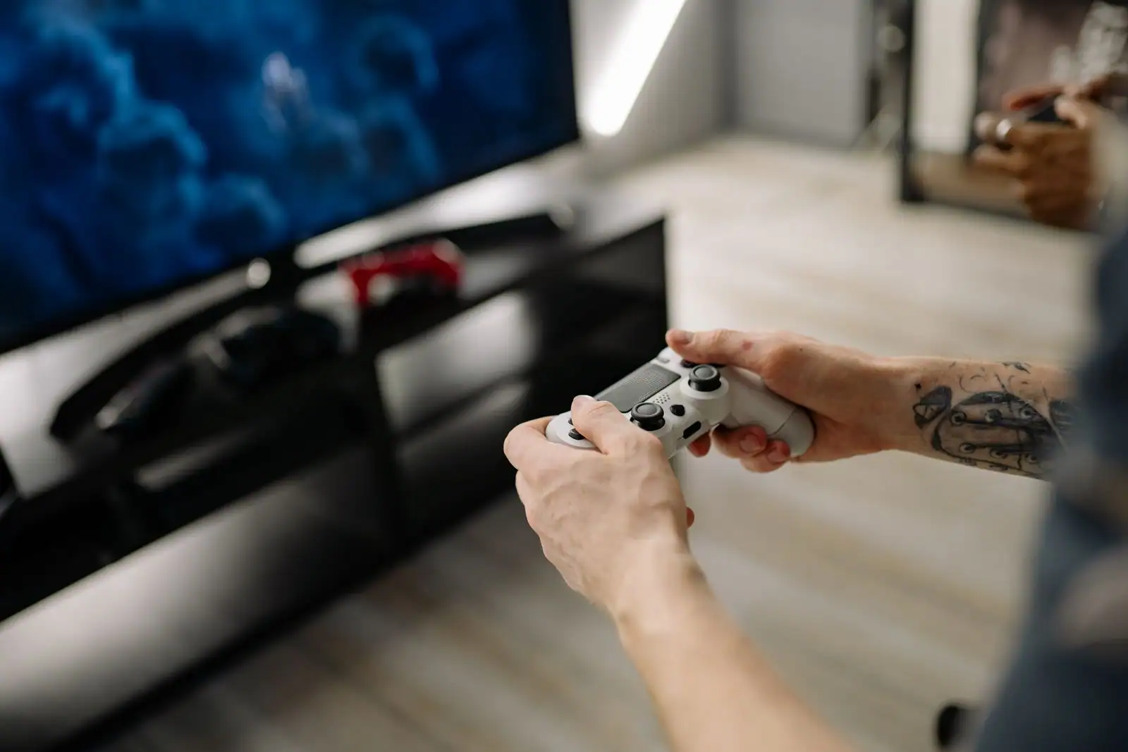 Mains tenant une manette de jeu blanche devant un téléviseur affichant un jeu vidéo dans un salon