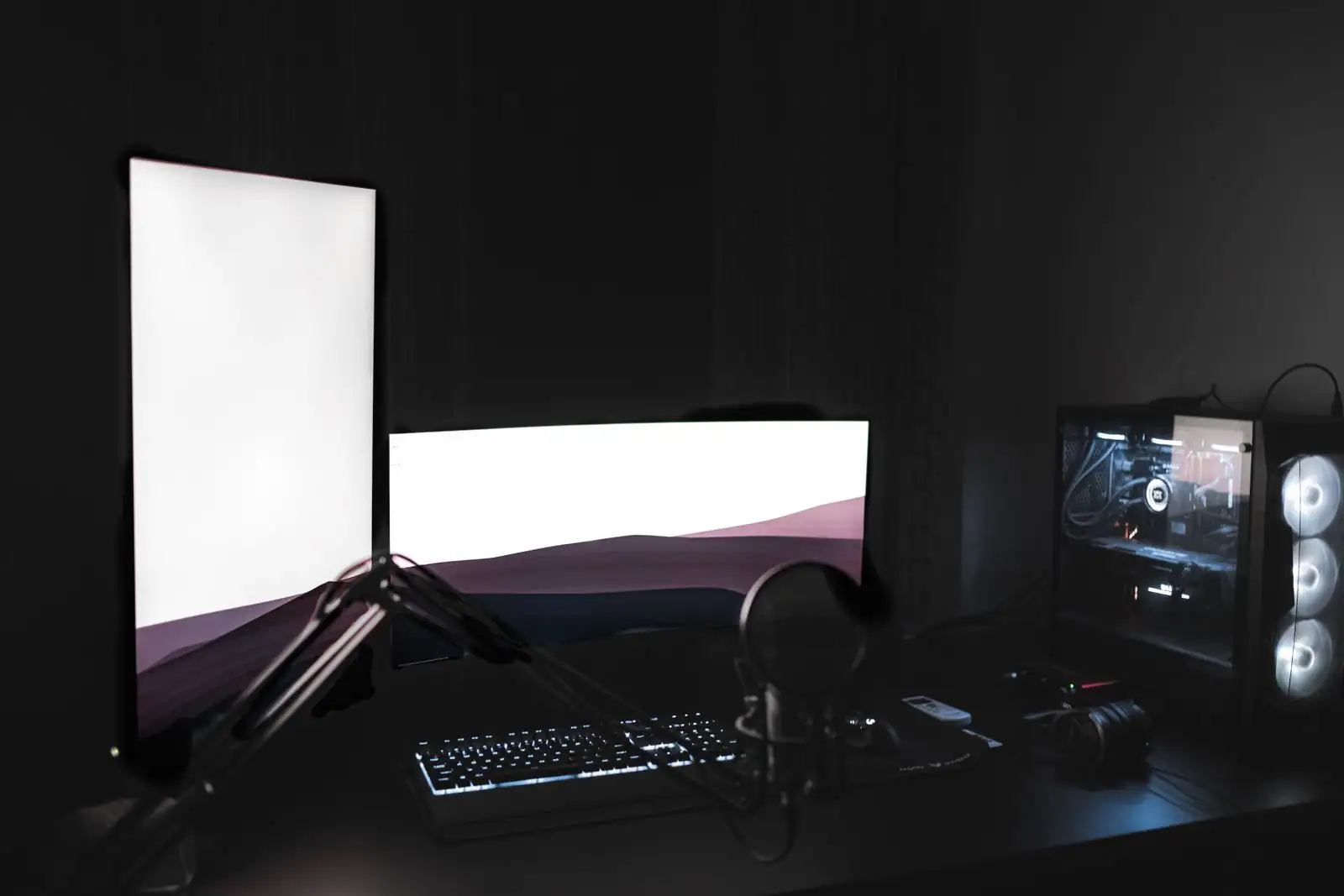 Poste de streaming dans une pièce sombre, micro sur bras articulé, clavier rétroéclairé et écrans allumés.