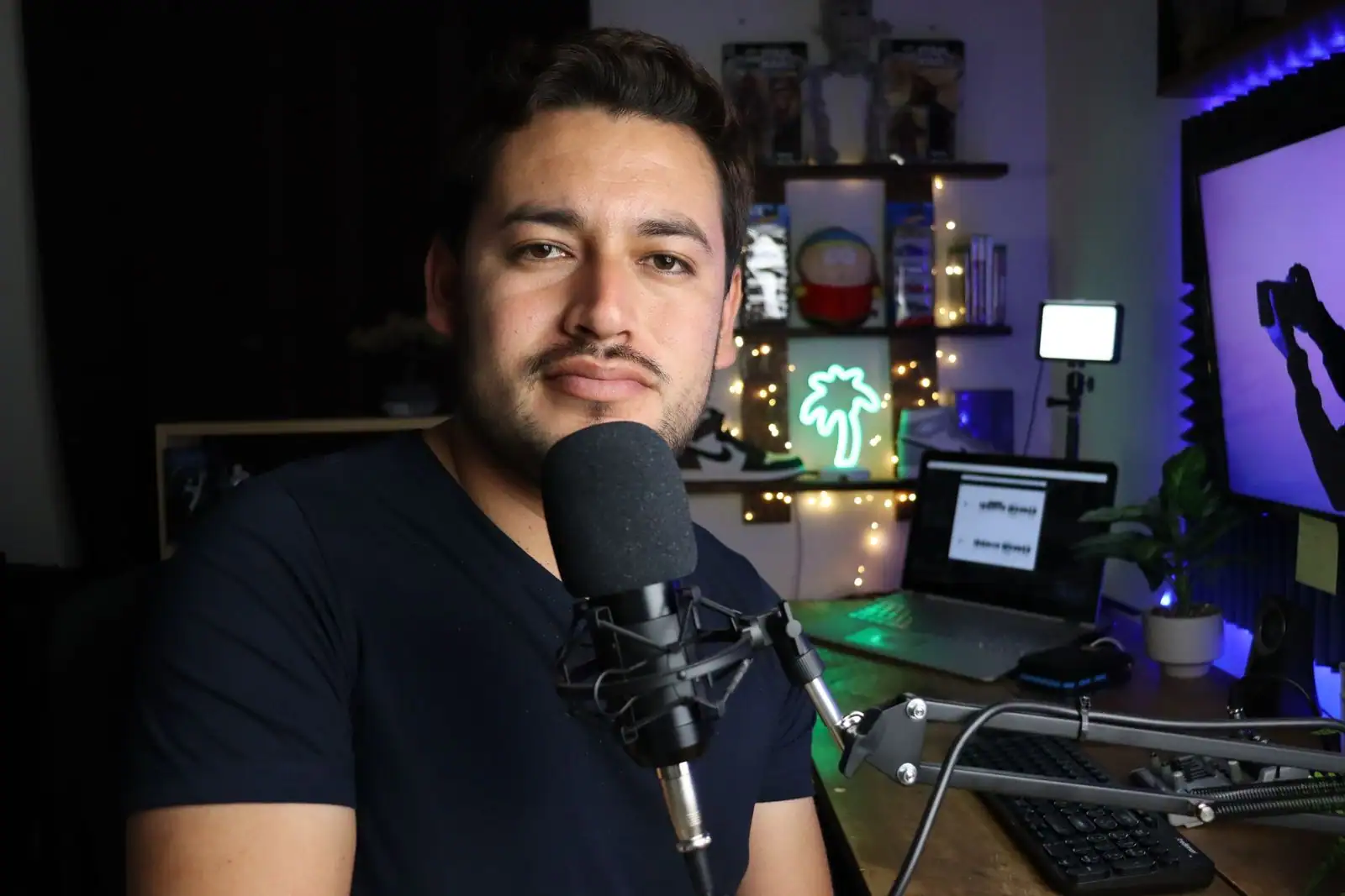 Créateur de contenu assis à un bureau de streaming face à un grand micro, dans une pièce sombre éclairée de néons.