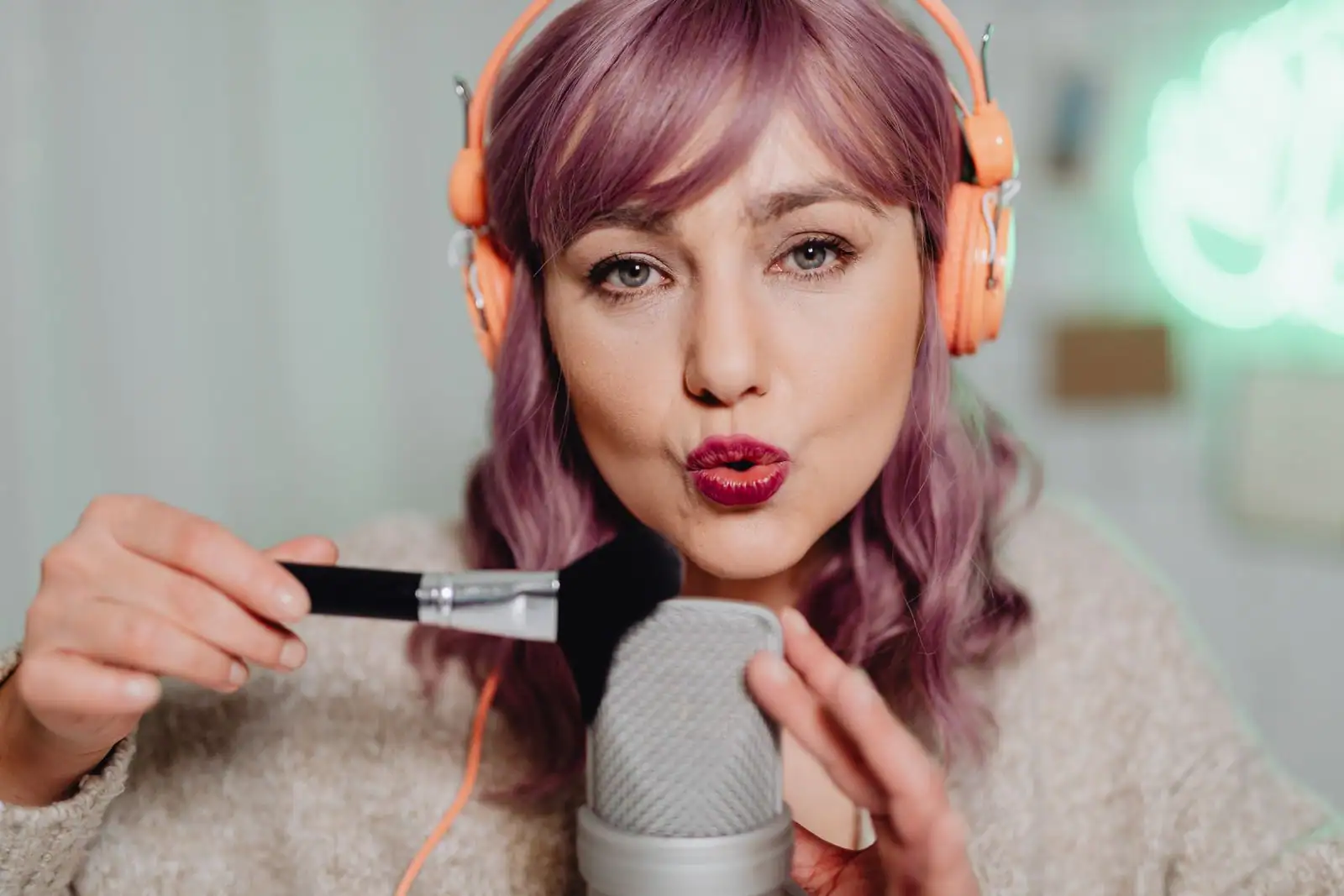 Femme avec un casque audio parlant dans un grand micro de studio, lumière néon en arrière-plan.