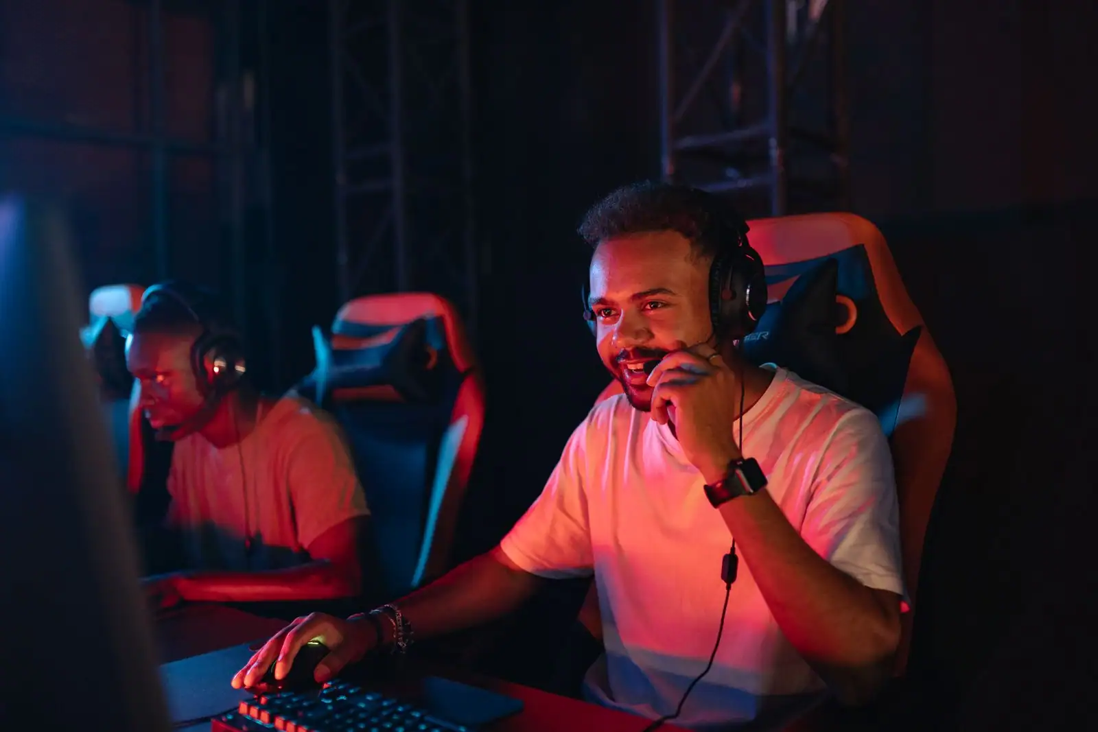 Joueur souriant avec casque et micro devant son écran dans une salle de jeu éclairée au néon