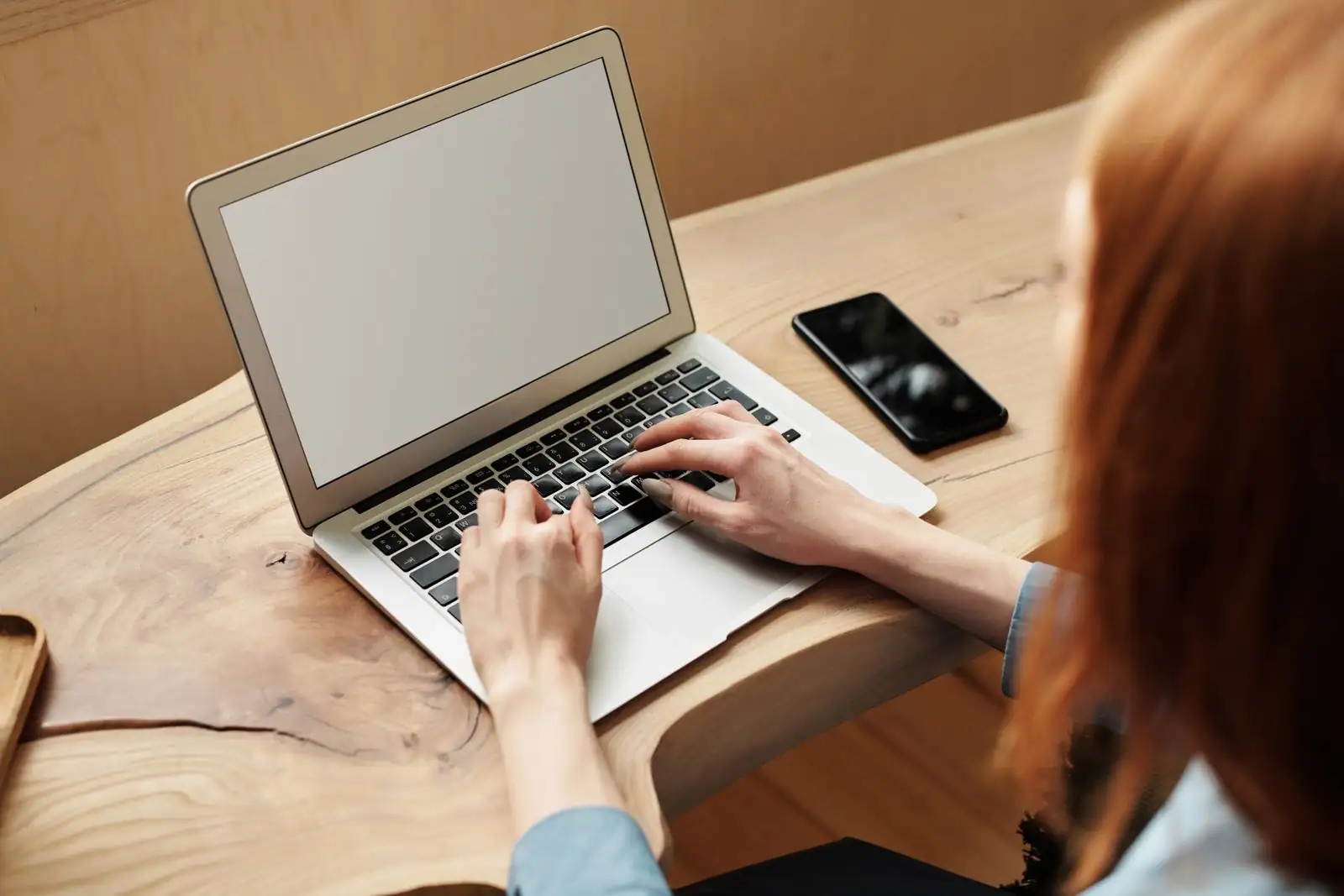 Personne tapant sur un ordinateur portable posé sur un bureau en bois, un smartphone à côté