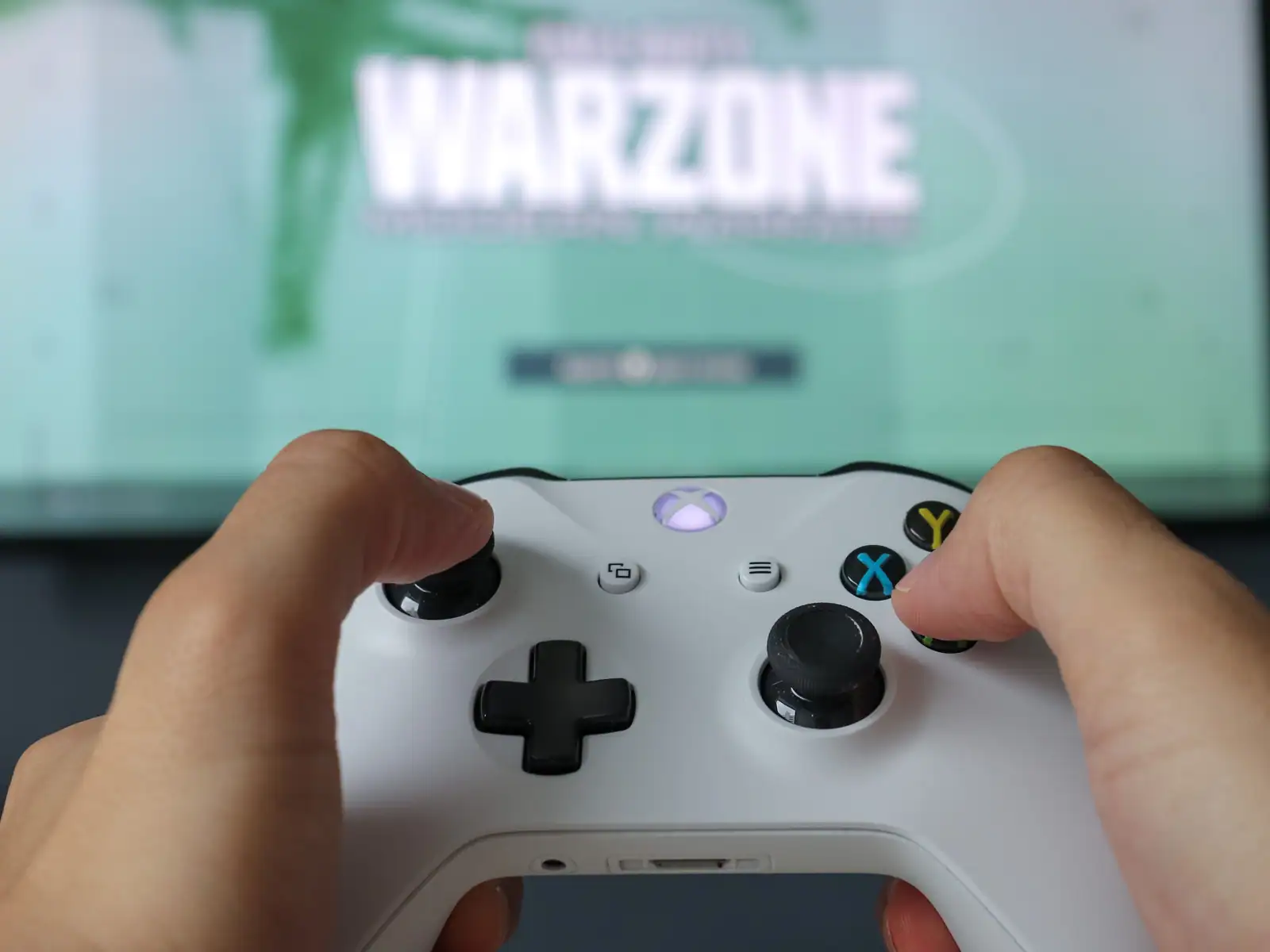 Manette Xbox blanche tenue à deux mains devant un téléviseur affichant un jeu vidéo en cours