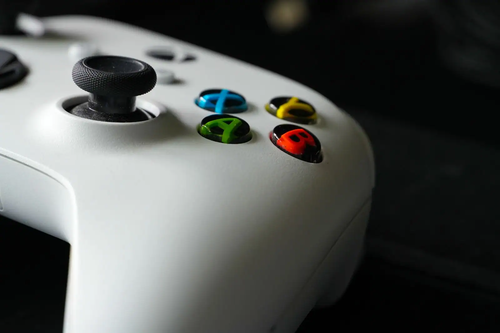 Gros plan sur une manette de jeu Xbox blanche et ses boutons colorés sur fond sombre.