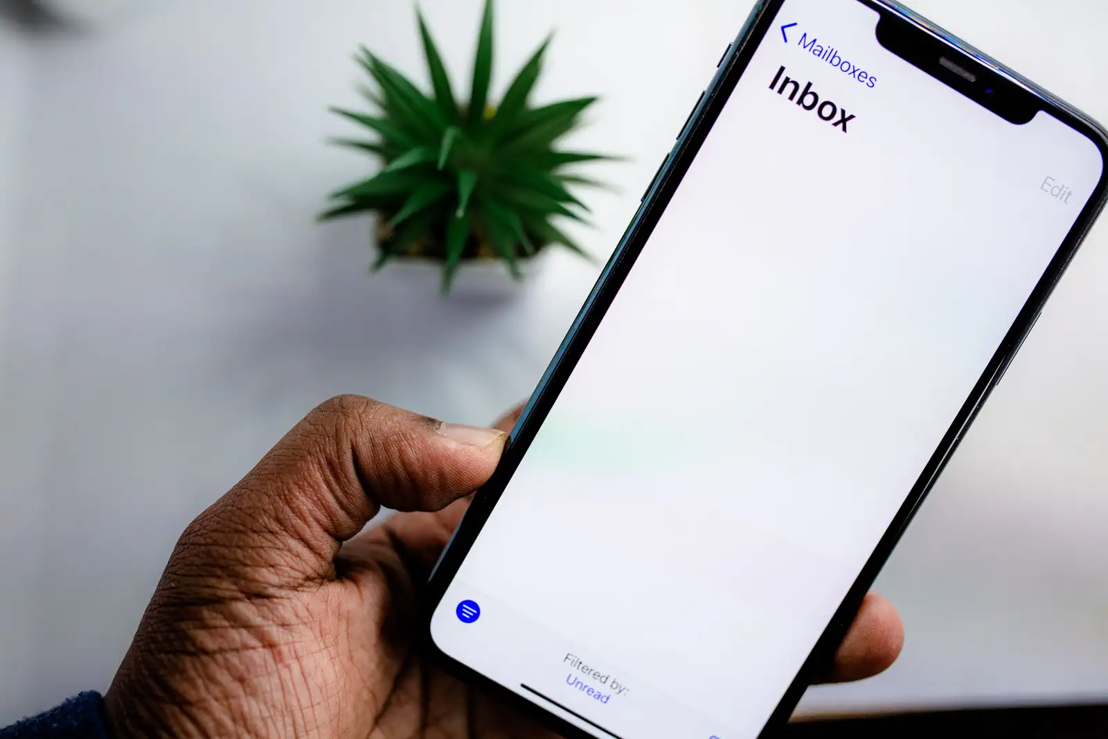 Une main tient un smartphone affichant la boîte de réception d’une messagerie.