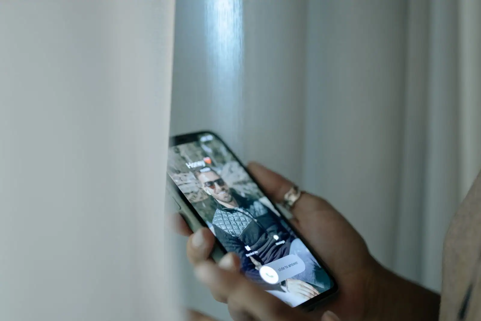 Une main tient un smartphone dont l'écran affiche un appel entrant en cours.