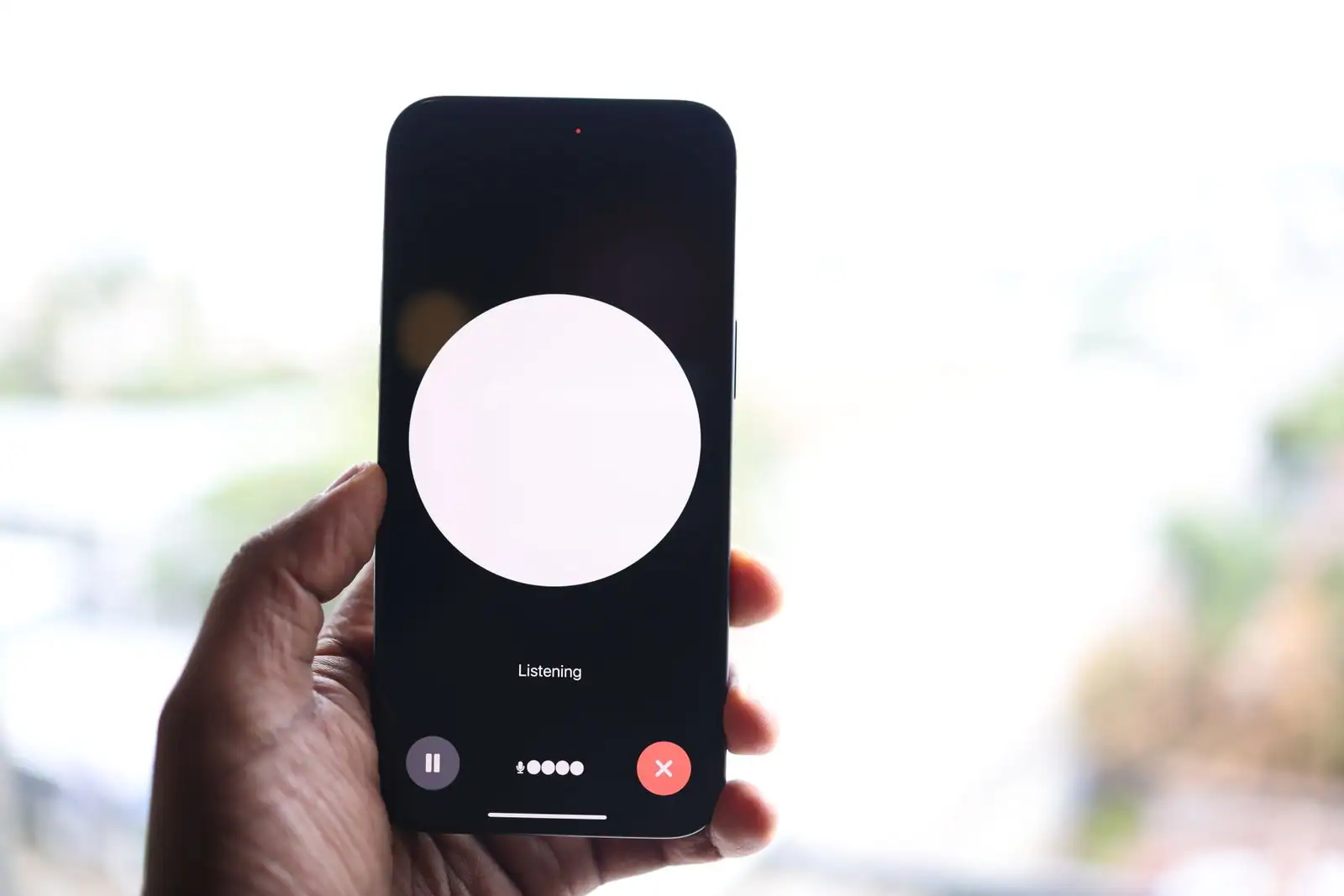 Main tenant un smartphone affichant l’interface d’un mode vocal en écoute, avec un halo lumineux au centre.