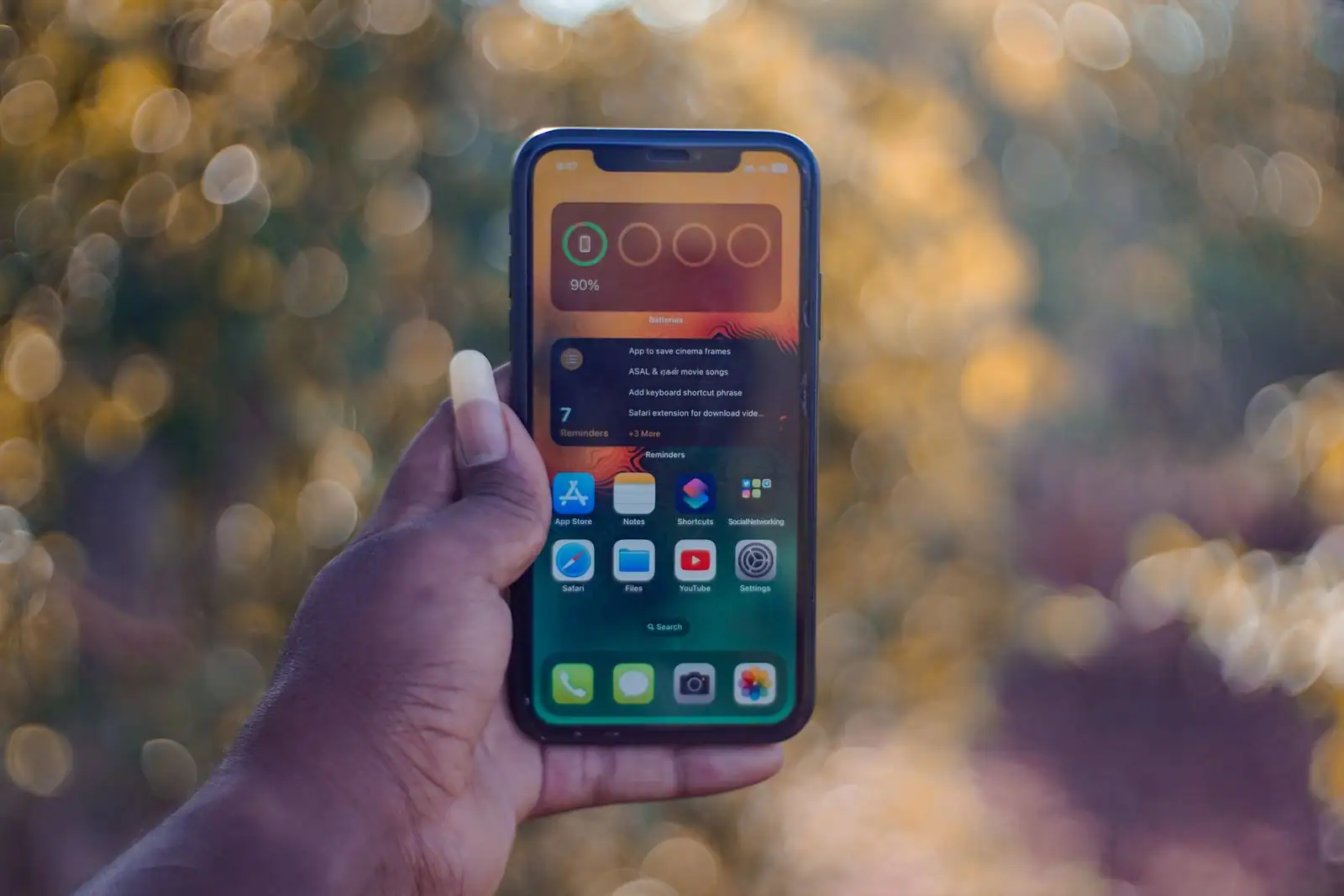 Main tenant un smartphone dont l'écran d'accueil affiche des icônes sur un fond coloré