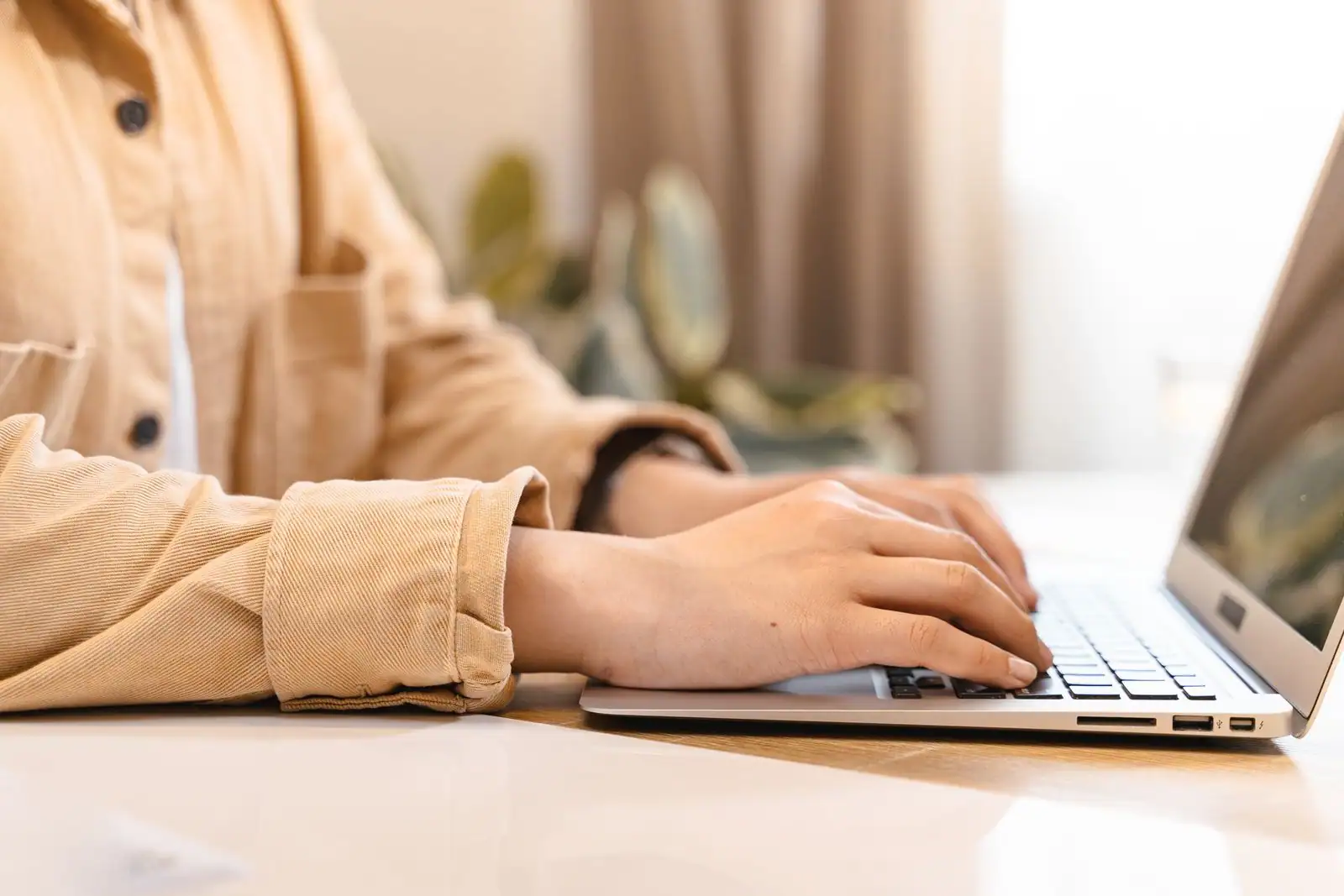 Une personne sur son ordinateur portable, les mains sur le clavier, dans un intérieur lumineux.