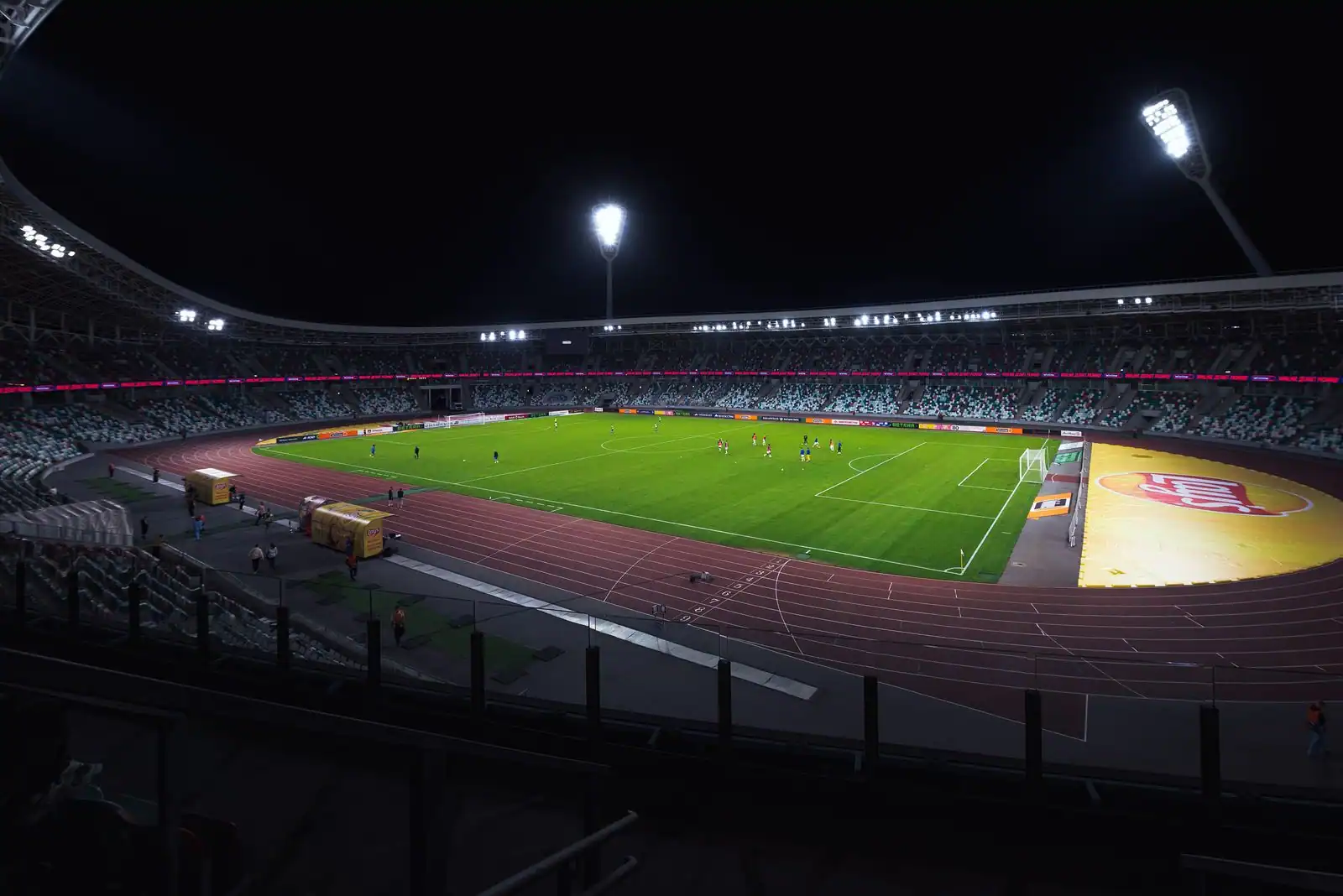 Match de football dans un stade illuminé la nuit sous les projecteurs, joueurs sur la pelouse.