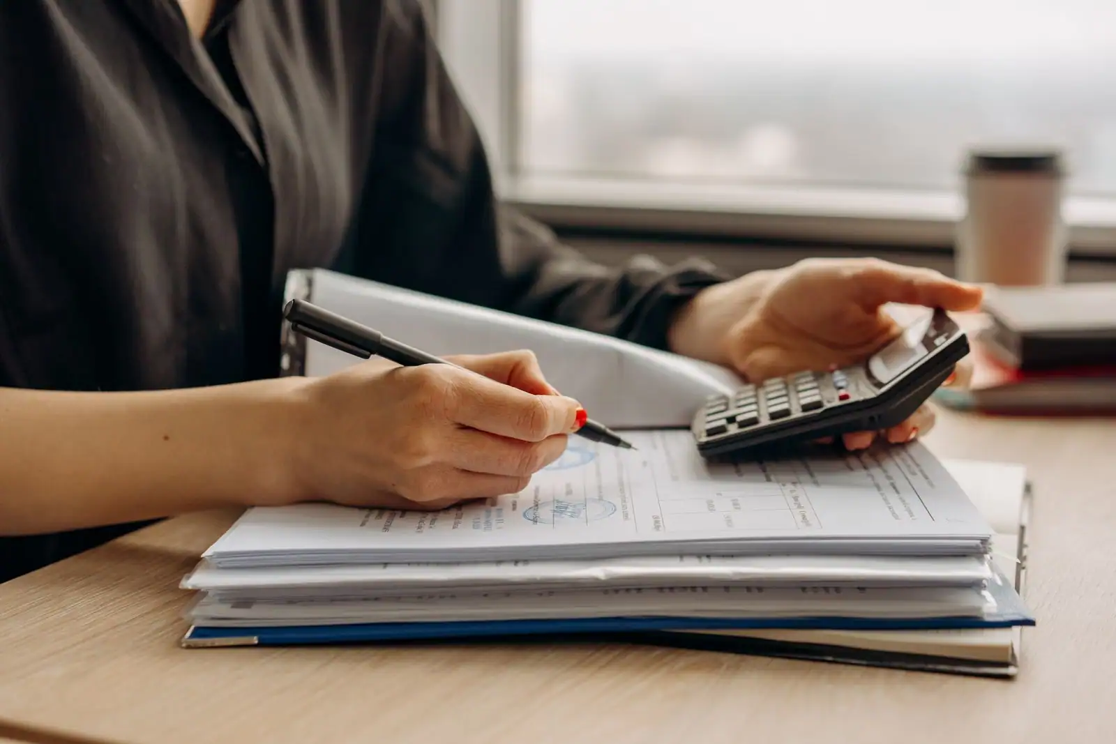 Une personne annote des documents chiffrés à côté d’une calculatrice, comme pour vérifier des remboursements.