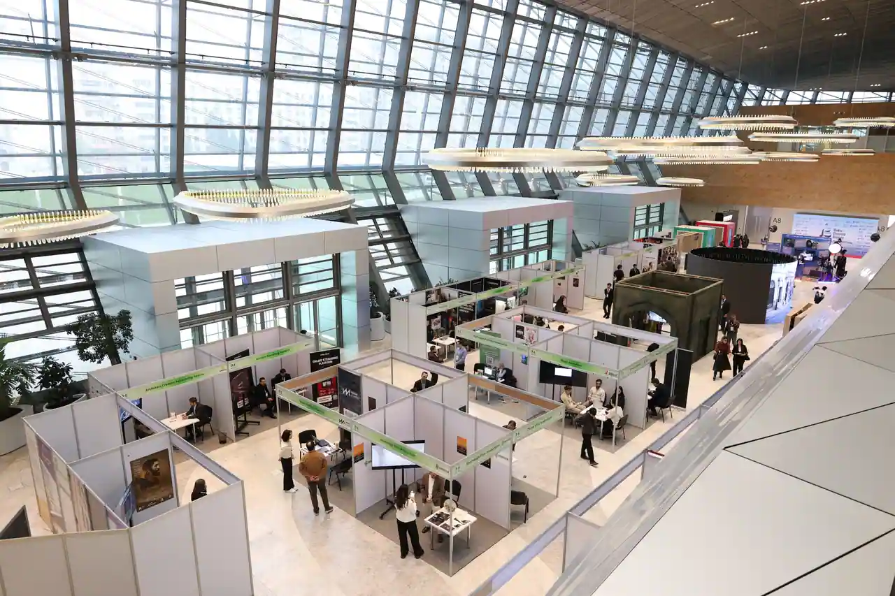 Vue plongeante sur les stands et les visiteurs d'un salon professionnel installé dans un grand hall vitré.
