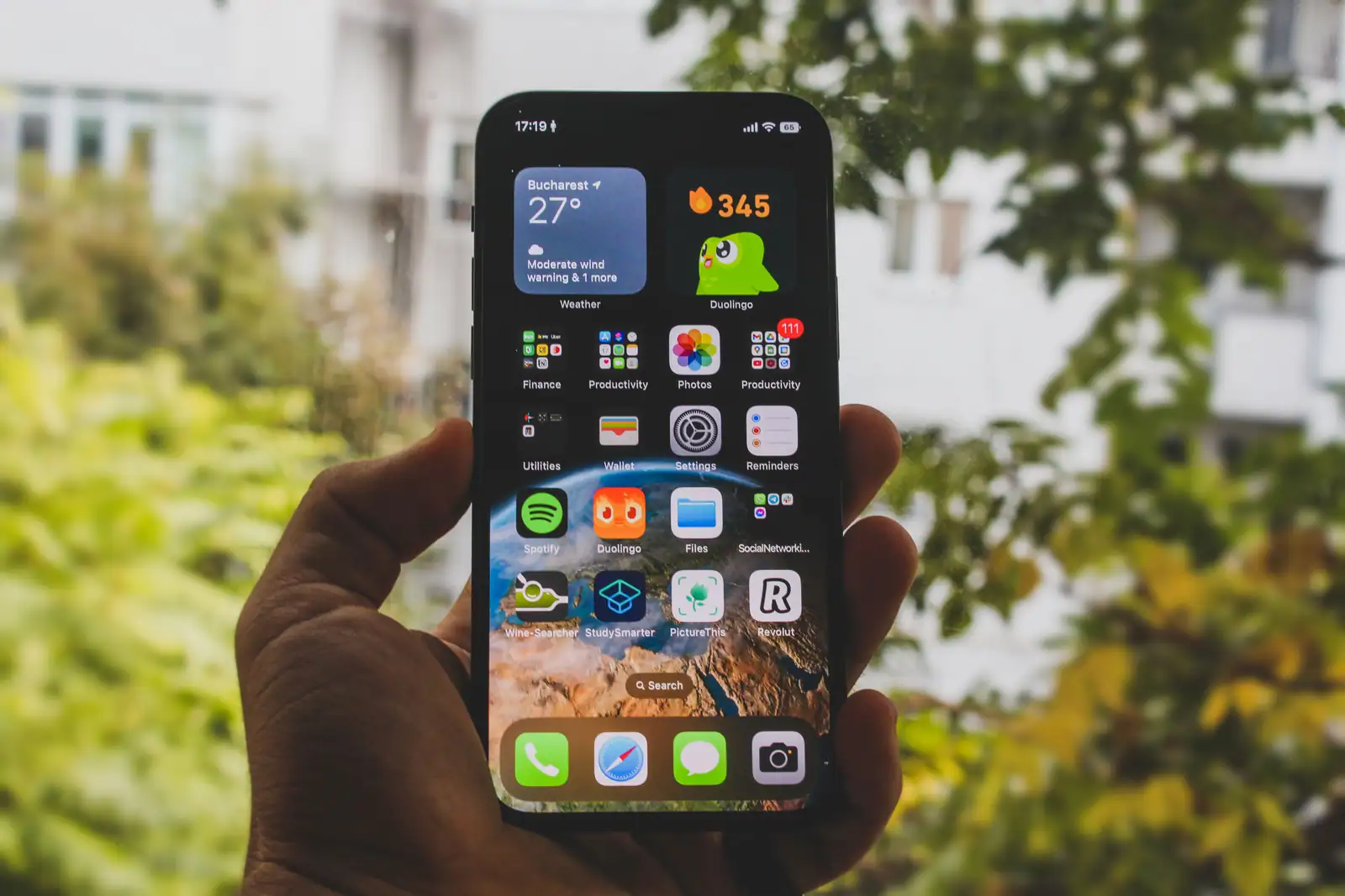 Un smartphone tenu à la main en extérieur, un widget météo affiché en haut de son écran d'accueil.
