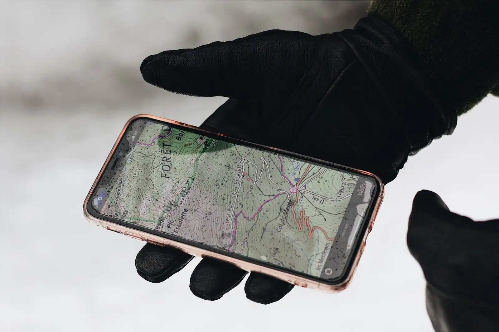Main gantée tenant un smartphone affichant une carte topographique de montagne, par temps de neige