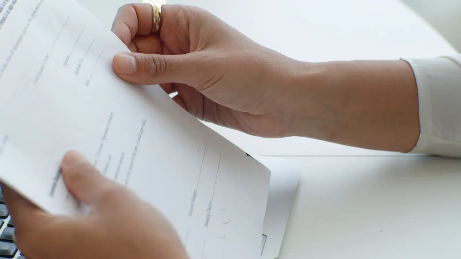 Mains tenant des feuilles imprimées au-dessus du clavier d'un ordinateur portable, en relecture.