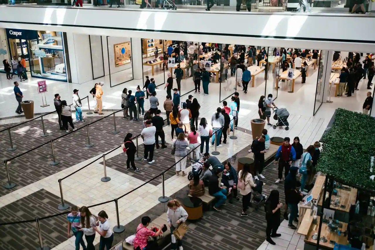 File d'attente encadrée de barrières devant une boutique Apple, dans la galerie d'un centre commercial.