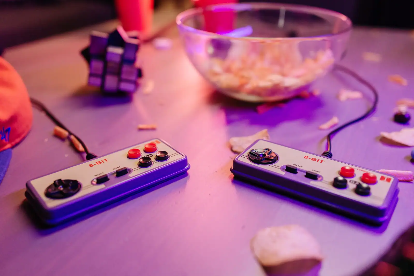 Deux manettes de jeu rétro posées sur une table, dans la lumière violette d'une soirée de jeu