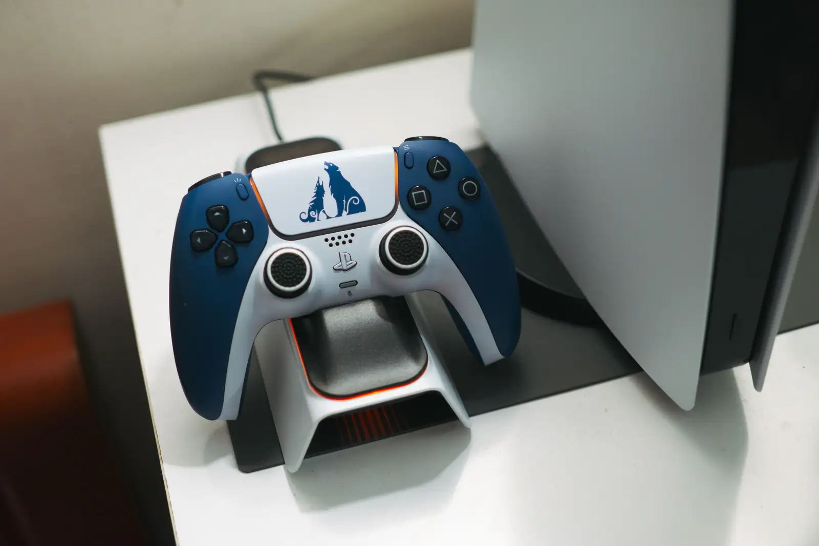 Manette DualSense posée sur son socle de charge à côté d'une console PlayStation 5 blanche.