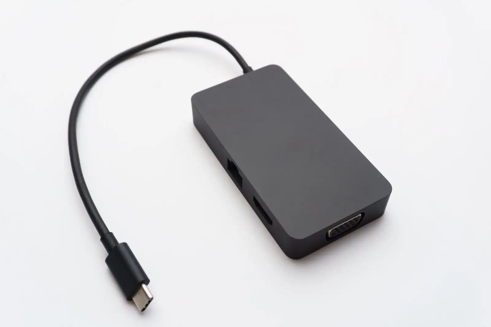 Adaptateur USB-C doté de ports Ethernet, HDMI et vidéo, relié à son connecteur, posé sur fond clair.